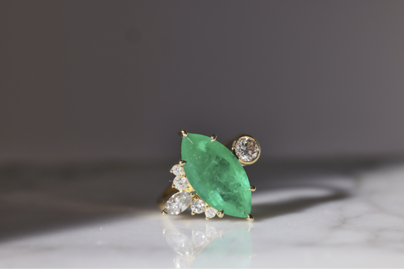 A Marquise Cut Light Green Diamond Ring placed on shiny surface with black background