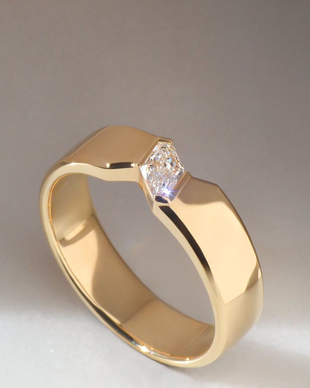 18ct yellow gold ring with a single lozenge cut diamond set diagonally in the centre, photographed on a neutral grey background.