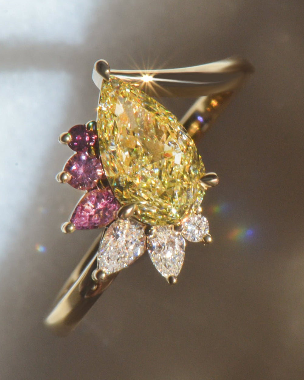 Gold ring with a pear cut yellow diamond, with pink sapphires and white diamonds on a marble grey background