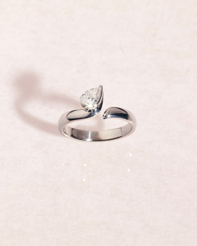 18ct white gold ring with a pear cut diamond on a light pink background