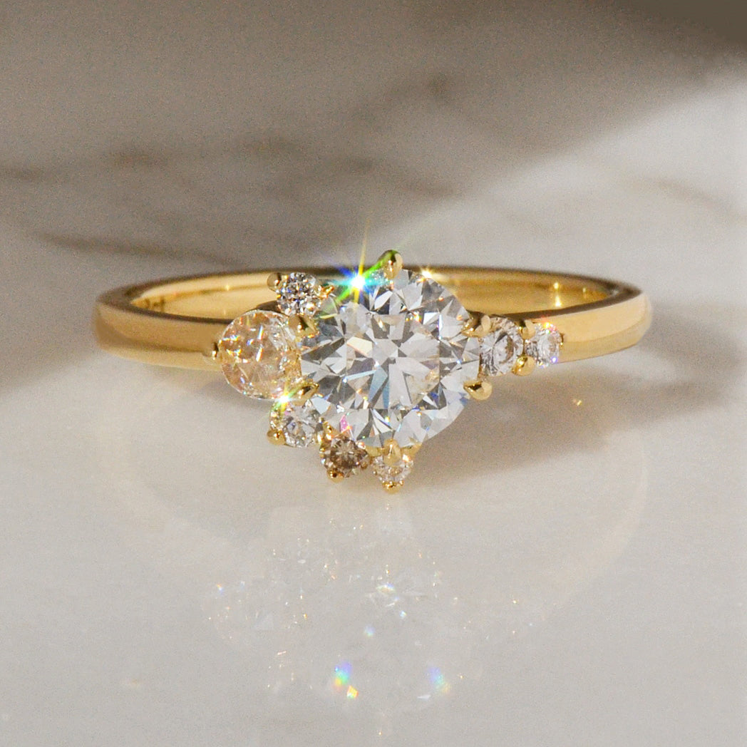 18ct yellow gold ring with a round diamond and smaller diamonds on a light background for Aesha Scott - by Layla Kaisi Collection