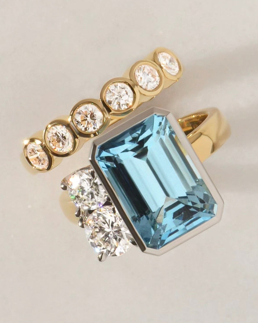 18ct yellow Gold ring with an emerald cut aquamarine centrestone and smaller round diamonds set in platinum. Paired with a round diamond wedding ring