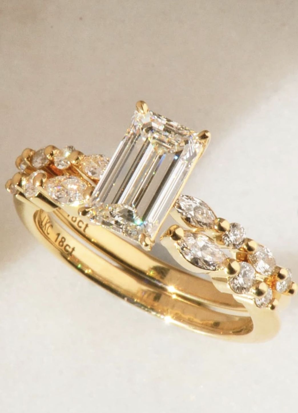 Gold ring with emerald-cut diamond and smaller diamonds on a light background