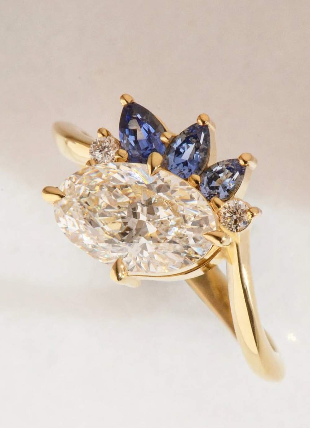 Gold ring with a oval cut diamond and smaller sapphire accent stones on a light background