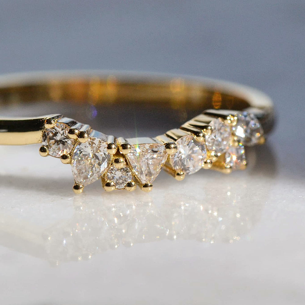 A close-up of a Pear and Round shaped Diamond Wedding Band placed atop a reflective white surface