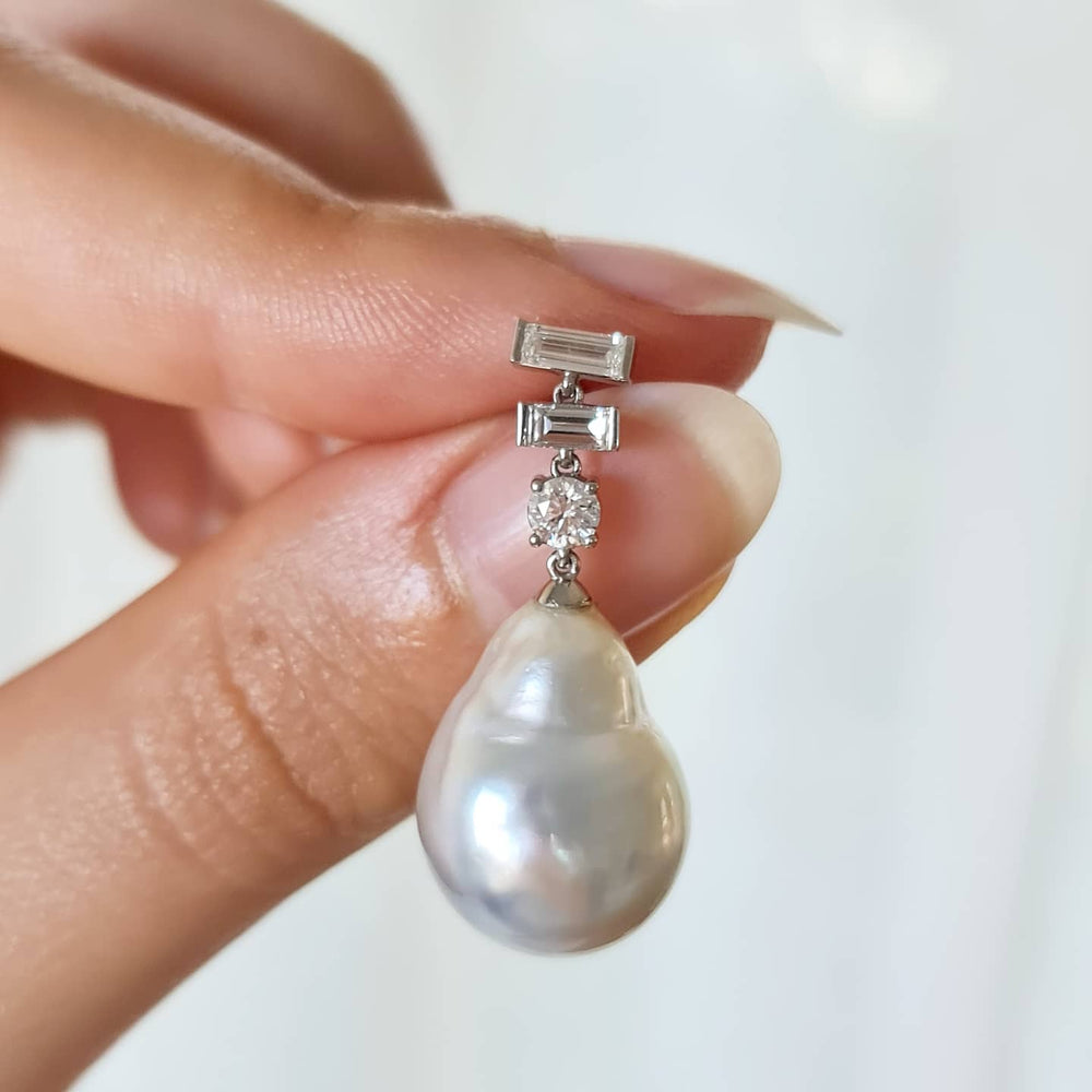 A close-up of two fingers holding a Diamonds Earring with Natural Baroque Pearl