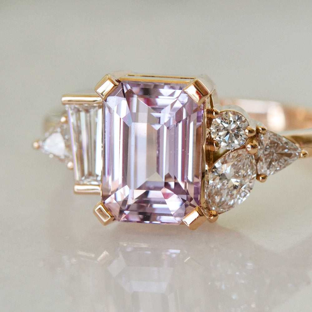 A Close-up of  a emerald cut pink Sapphire Diamond ring placed on a shiny surface