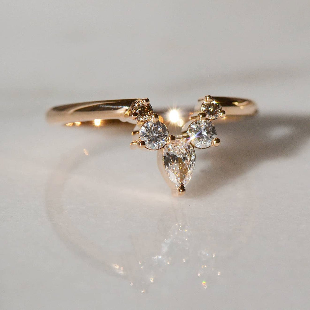 A close-up of a Pear and Oval shaped five stone Golden Engagement ring placed atop a shiny white surface
