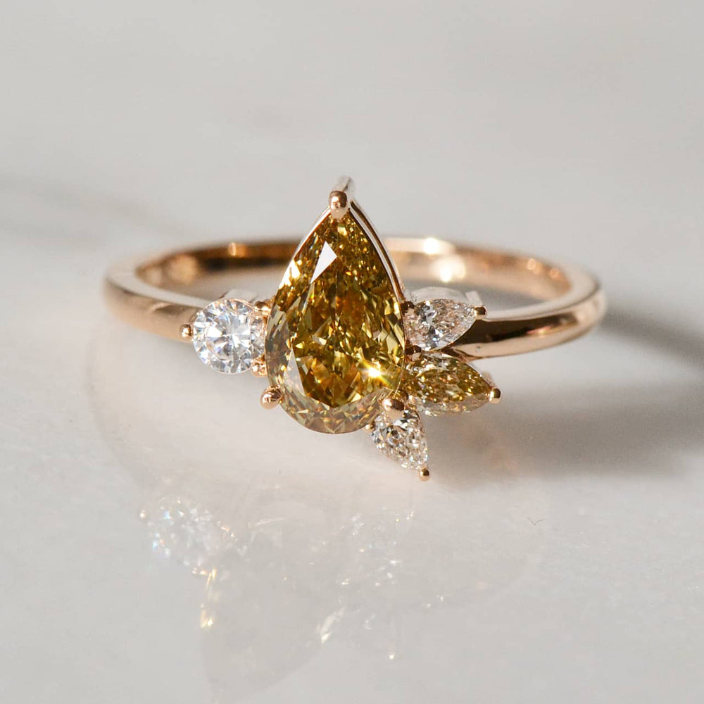 A stunning close-up of a Pear-shaped yellow diamond Ring atop a white shiny surface