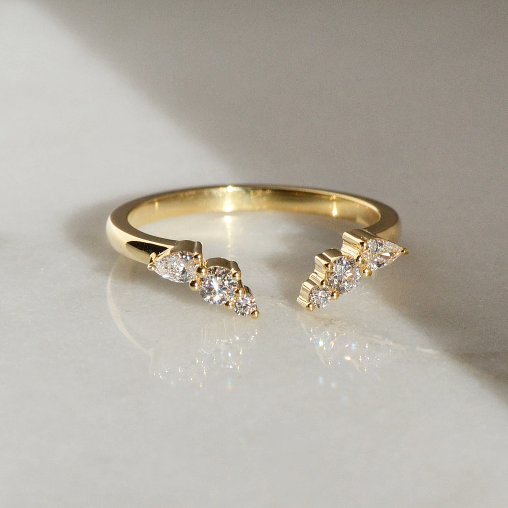 A closeup of a multi stone yellow gold minimalist diamond cluster Engagement Ring placed on a white shiny surface