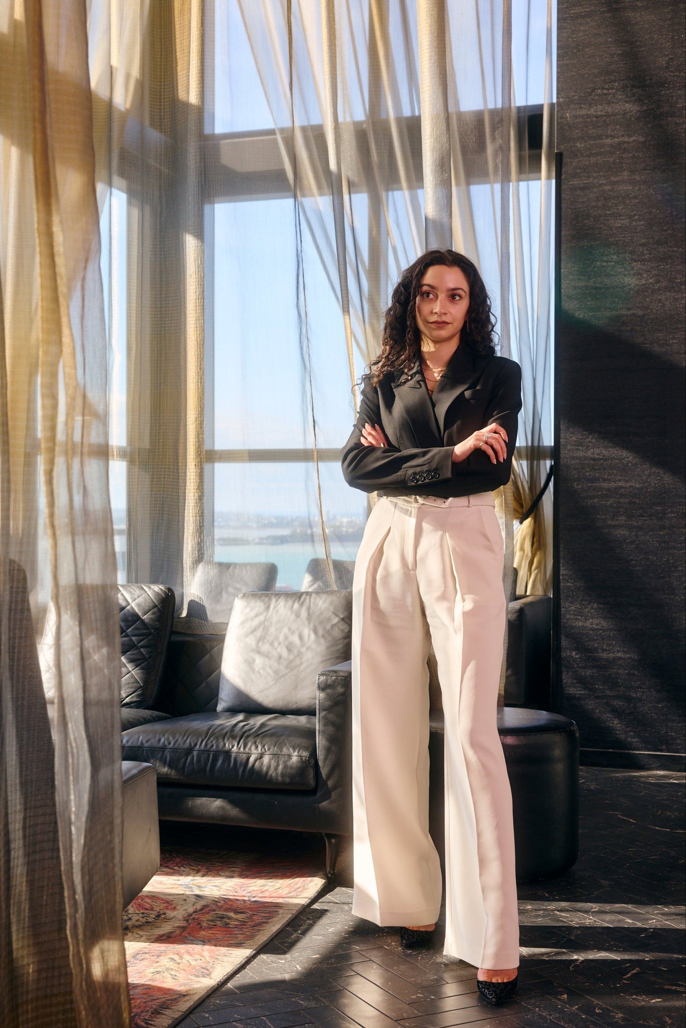 Woman standing in an elegant room with modern decor and large windows.