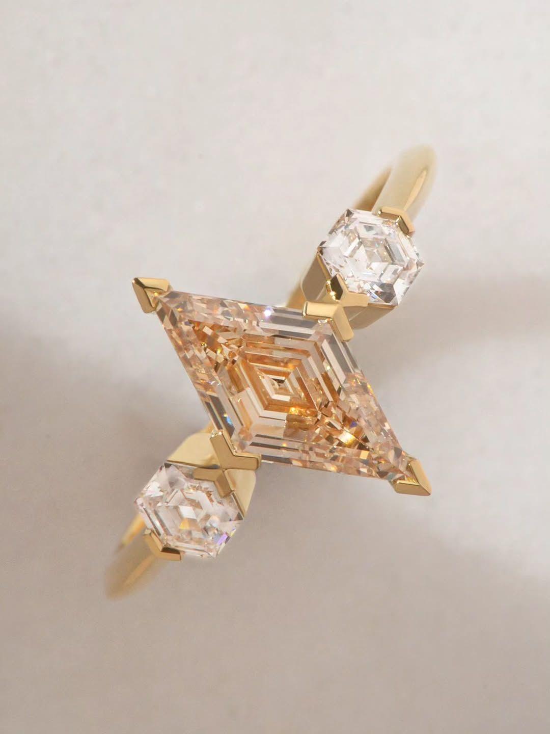 Bespoke trio diamond ring featuring a champagne lozenge cut diamond centrestone with two hexagonal cut accent stones, set in 18ct yellow gold, photographed on a light grey background