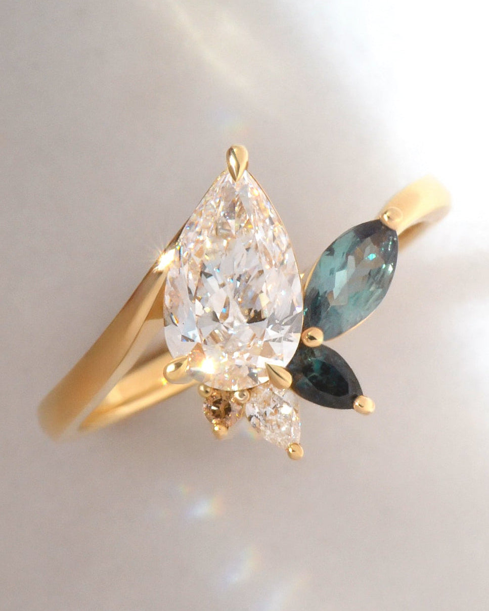 Ring with pear cut diamond and alexandrite, sapphire and diamond accents, set in 18ct yellow gold, on a white background