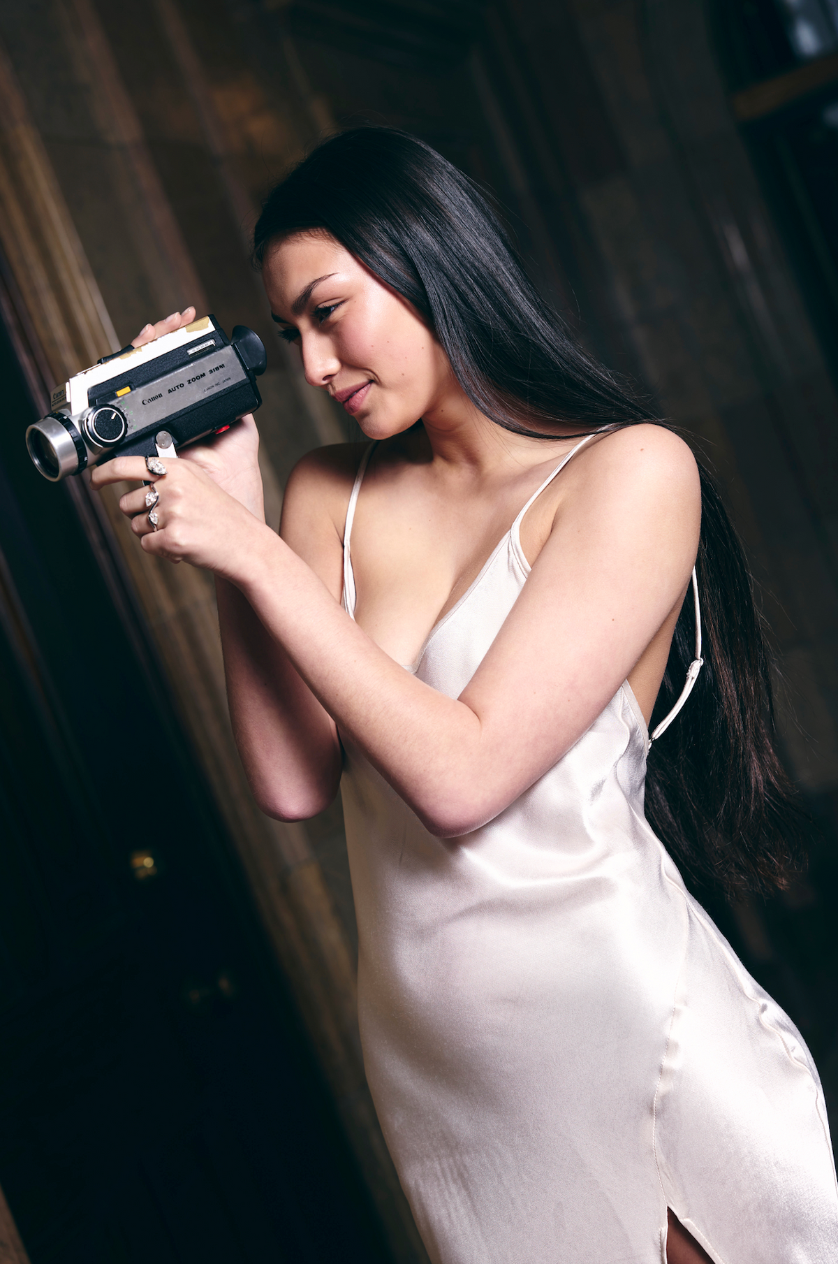 Woman in a white dress with three finger white diamond ring, holding a vintage 1970's Canon Super 8 film camera indoors