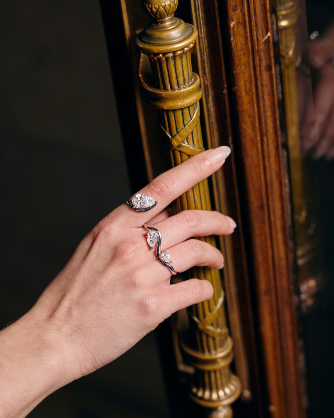 Hand with rings on a gold ornate door handle against a dark background