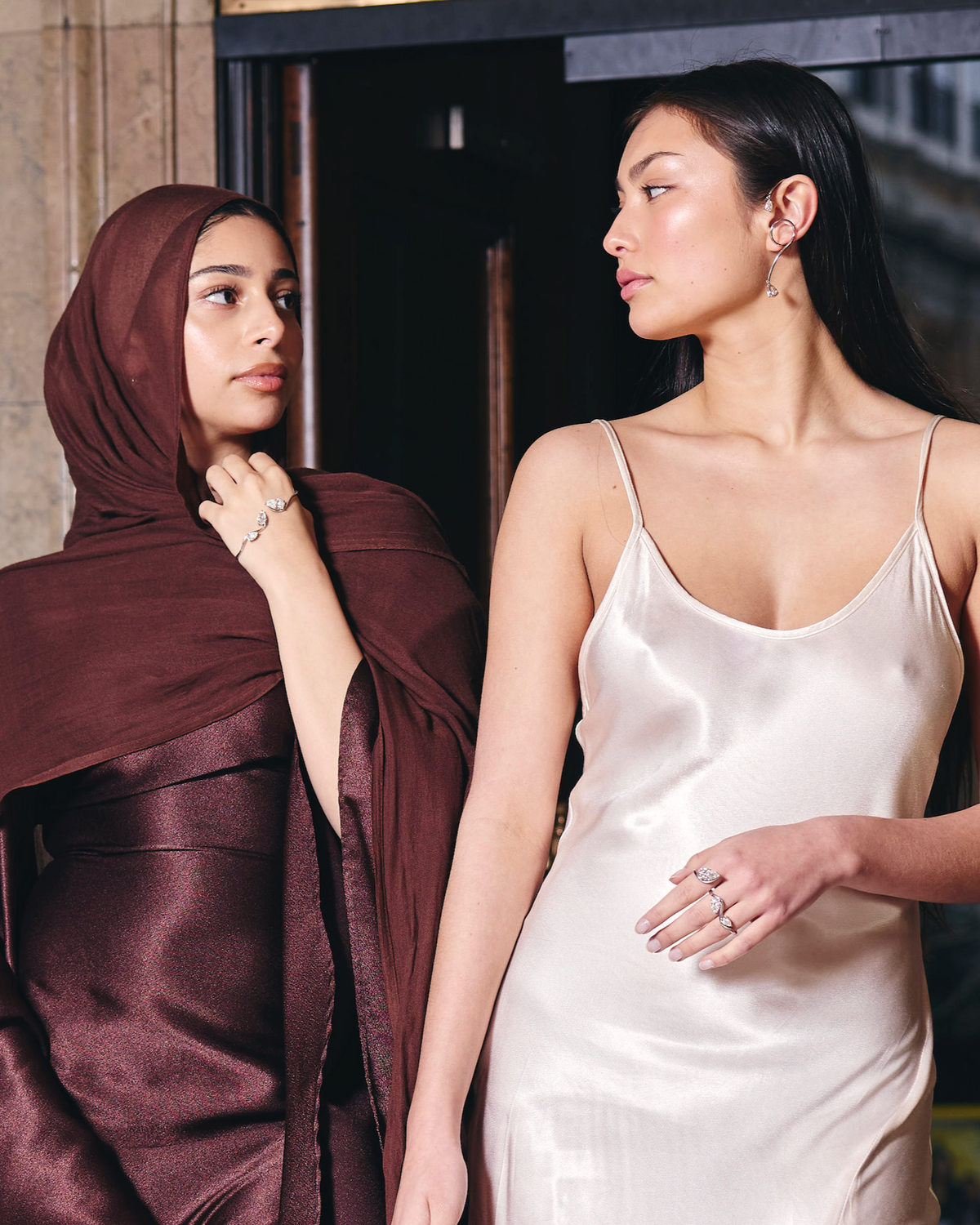 Two women wearing elegant dresses and diamond jewellery walking inside a marble hallway 