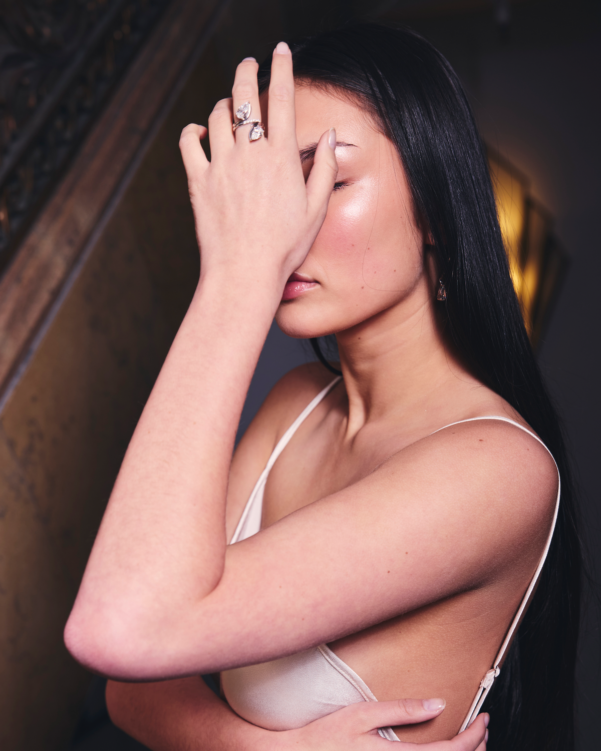 Woman in white slip dress holding her hand over her face to show two diamond earrings 