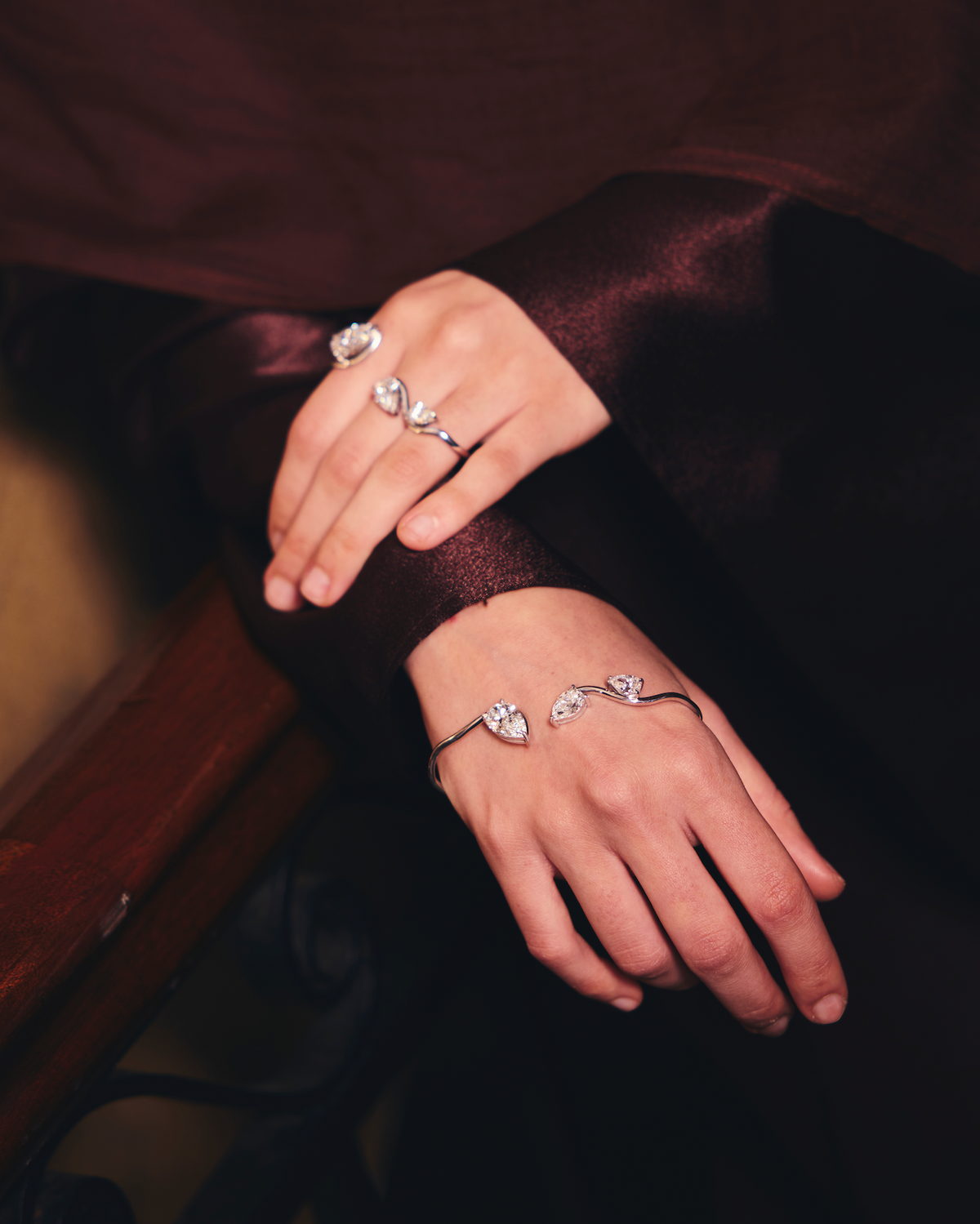 Close-up of hands wearing diamond rings and a diamond hand cuff on a dark background