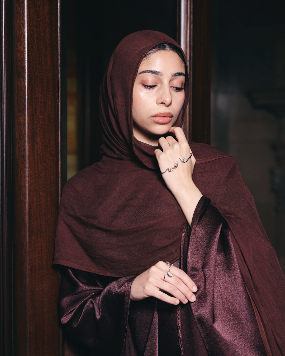 Woman wearing a dark brown hijab and dress, standing indoors.