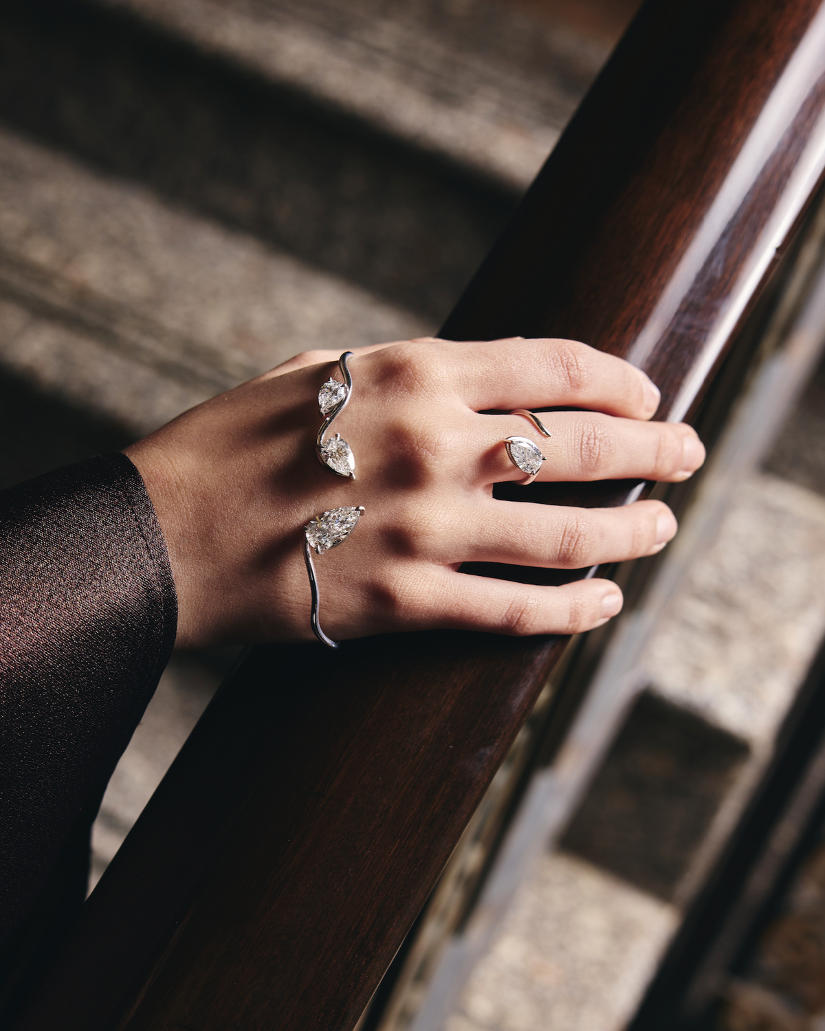 Hand with a diamond ring and diamond hand cuff on a wooden handrail