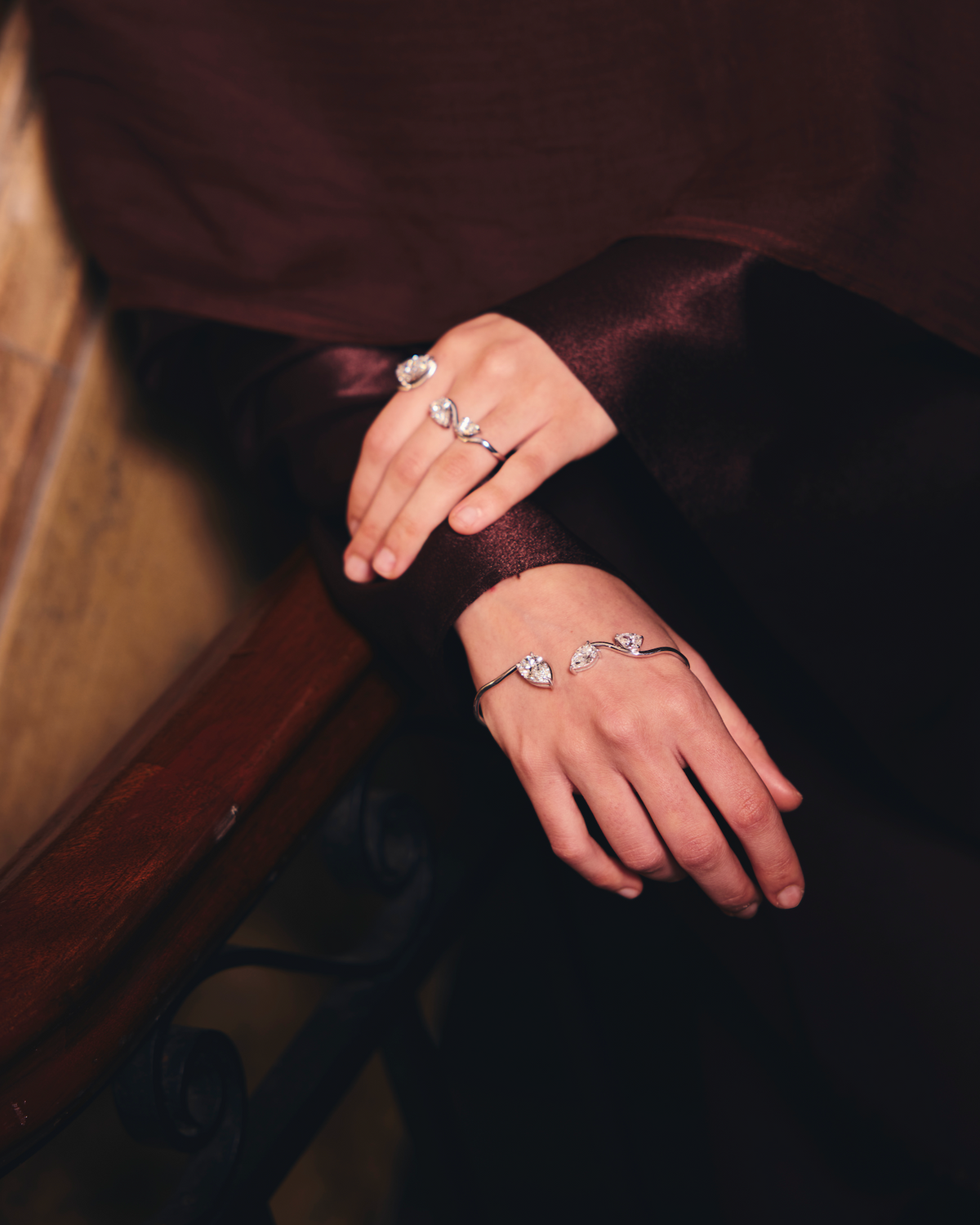 Close-up of hands wearing a three finger diamond ring and half cuff on a dark background