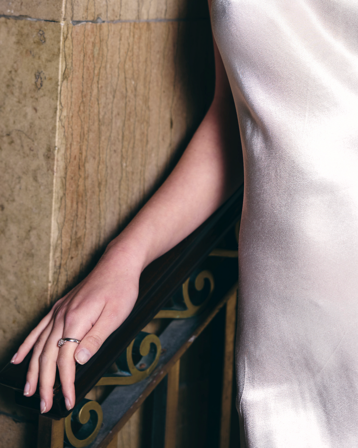woman wearing a silver dress with a close-up of their hand wearing a white diamond ring on a decorative railing.
