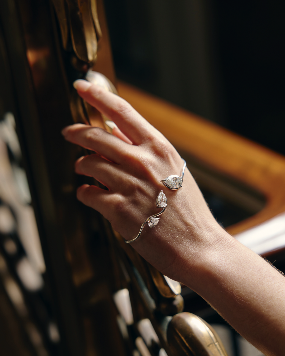 Hand wearing a diamond hand cuff on a wooden and brass handrail