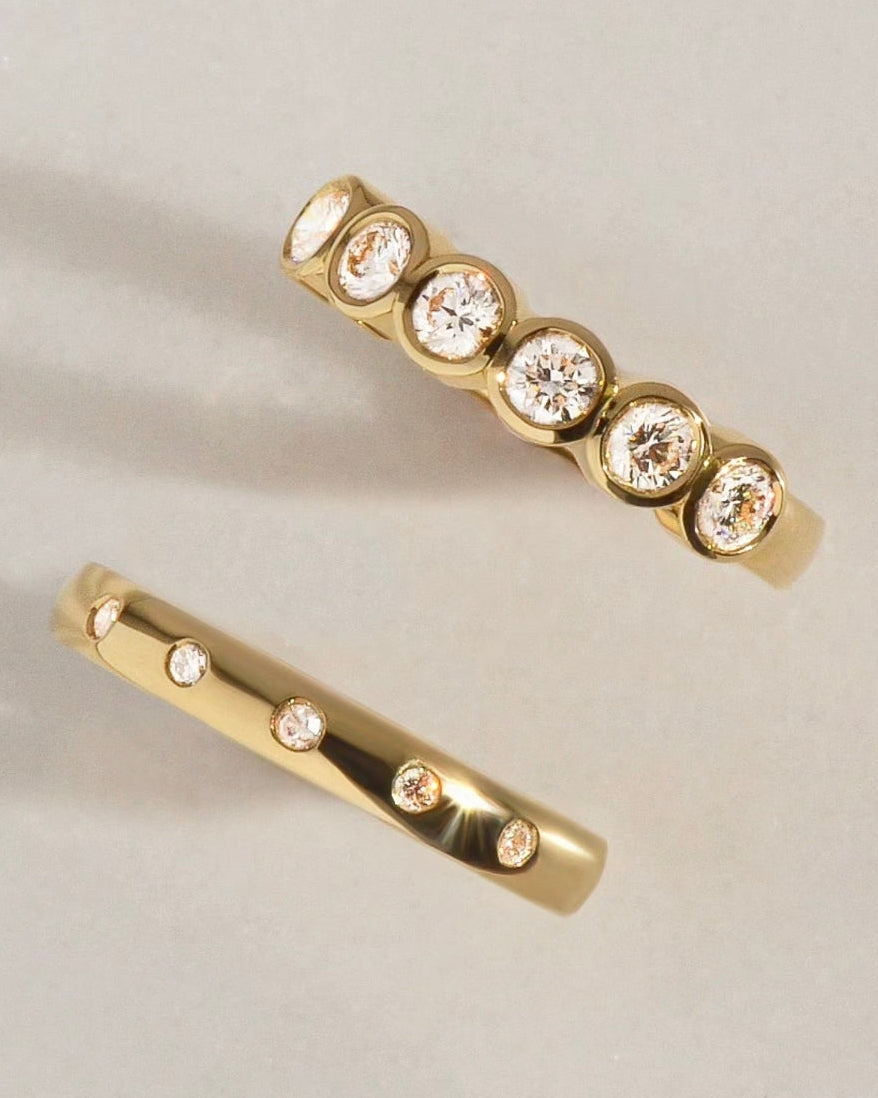 Two gold wedding rings with bezel set diamonds on a light beige background