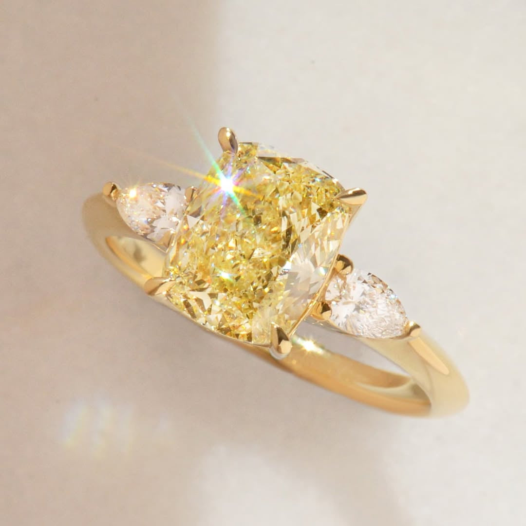 Gold ring with a cushion cut yellow diamond and pear cut white diamonds on a light background