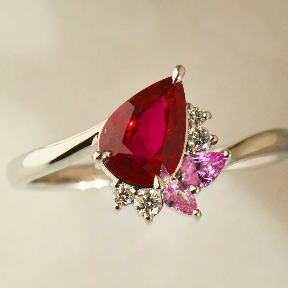 Pear cut ruby ring with diamonds and pink sapphires on a white background