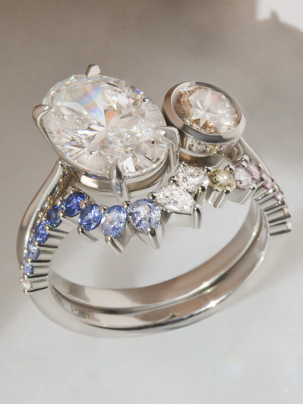 Elegant toi et moi engagement ring with large oval and round diamonds, paired with a matching bespoke wedding band with custom cut sapphires and diamonds,  on a light background