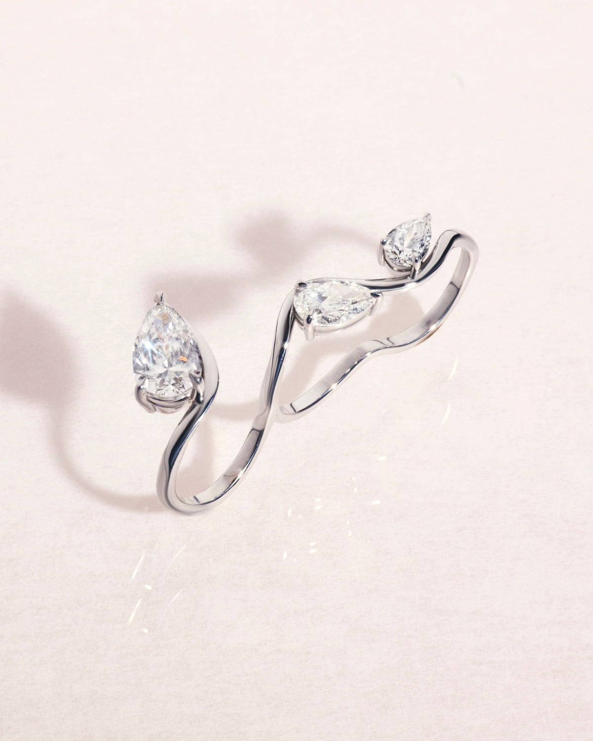 18ct white gold three-finger ring with pear cut diamonds on a light pink background