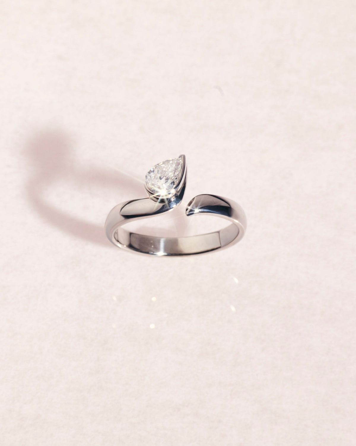 18ct white gold ring with a pear cut diamond on a light pink background