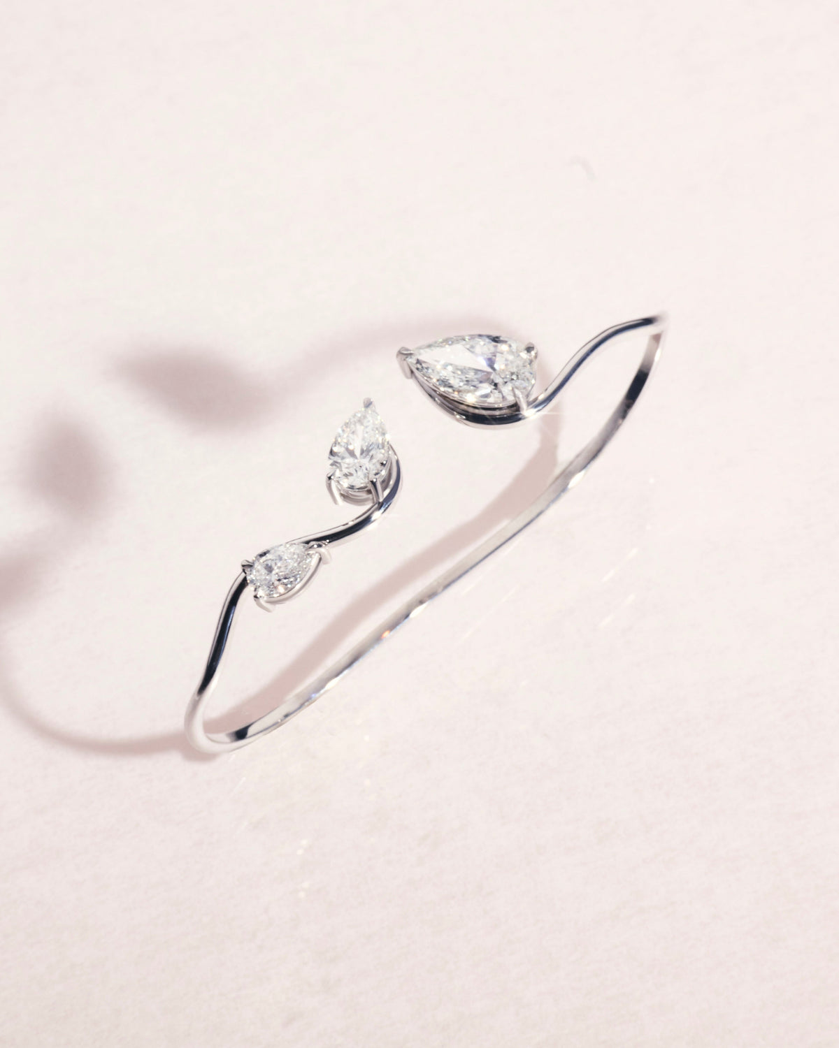 18ct white gold hand cuff with three pear cut diamonds on a light pink background