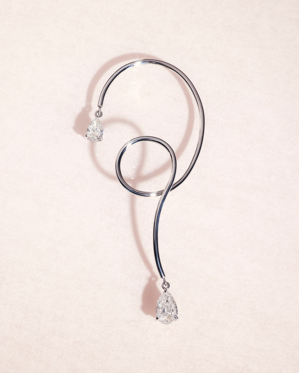 18ct white gold earring cuff with pear cut diamonds on a light pink background