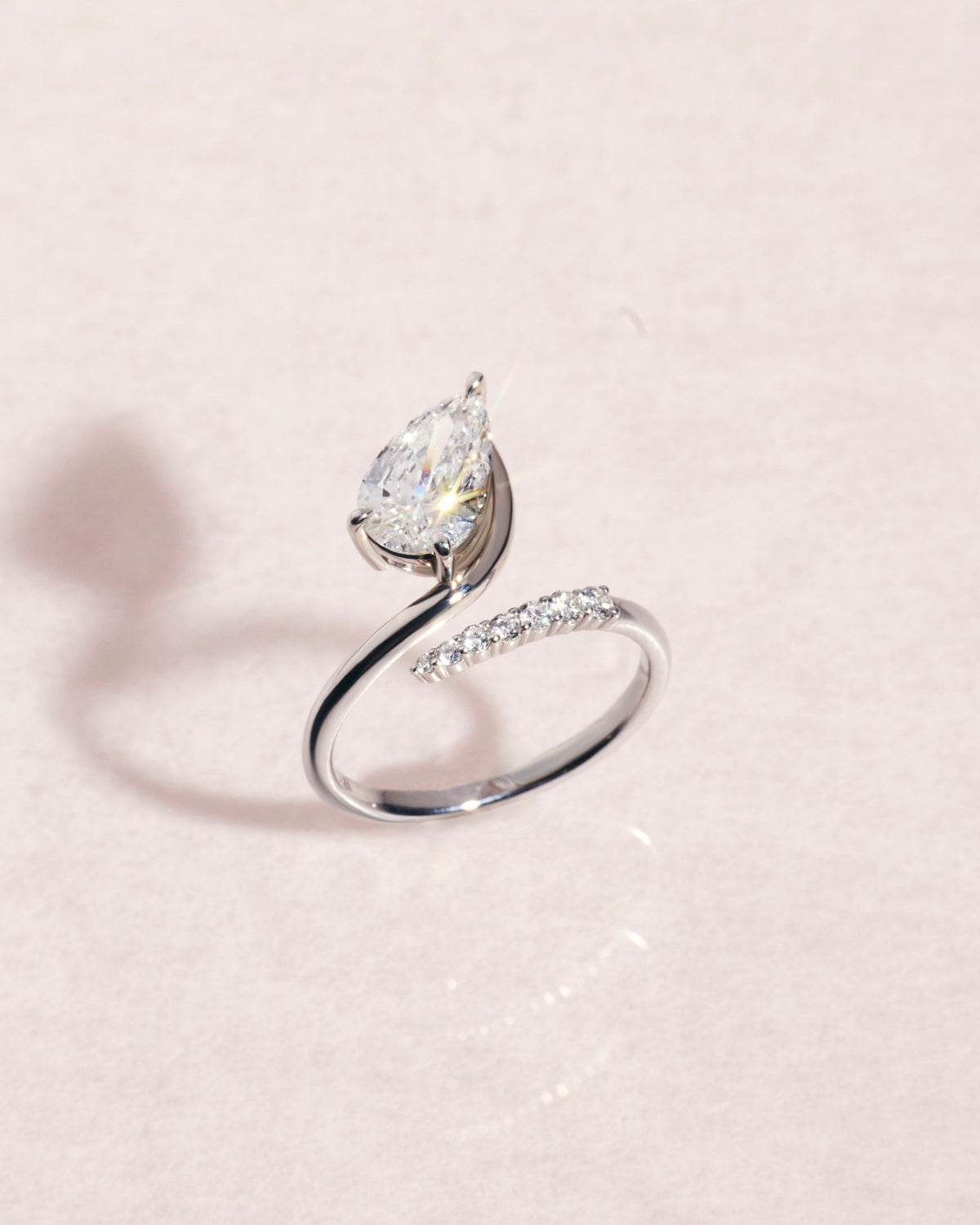 18ct white gold ring with a pear cut diamond on a light pink background