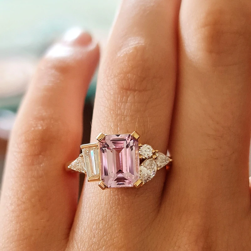 A close-up of a hand with an Emerald Cut Pink Sapphire Diamond ring on its finger